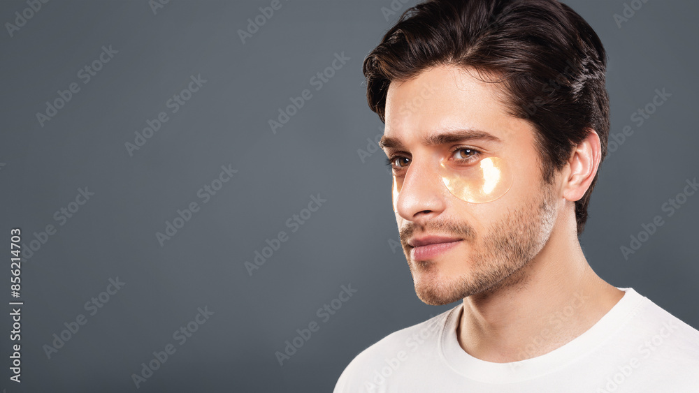 Fototapeta premium Young man with golden patches under eyes from wrinkles and dark circles, grey studio background