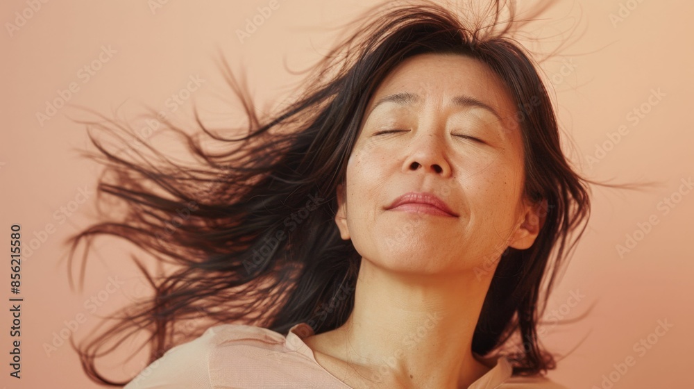 A woman with closed eyes enjoying a moment of tranquility her long dark hair flowing freely against a soft warm background.