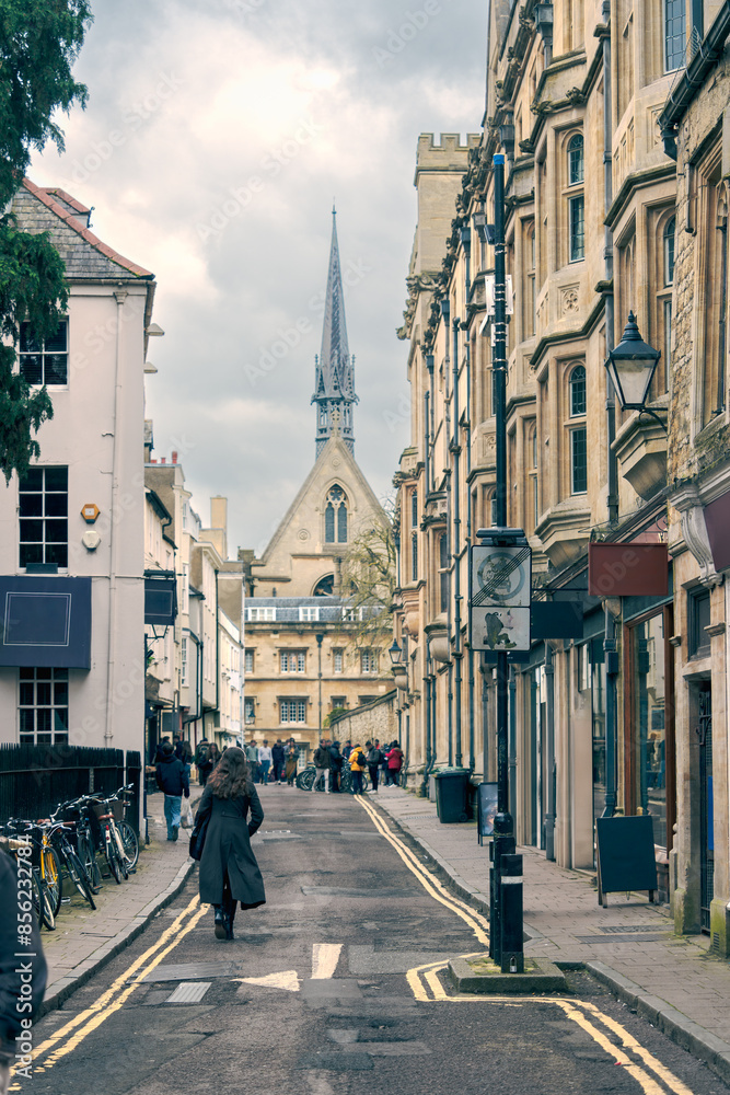 Obraz premium English street with Gothic architecture church spire and pedestrians capturing the charm of urban life and cultural richness, travel and lifestyle, focusing on historic beauty and city exploration