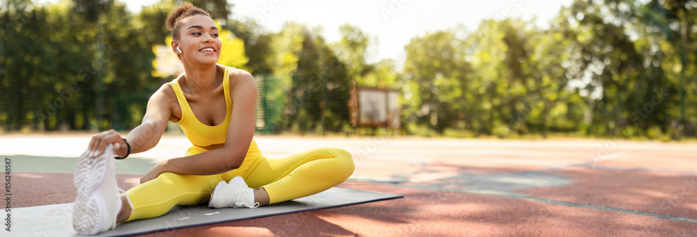 Sporty Lifestyle Concept. Smiling African American lady in yellow top, leggings and white sneakers stretching back, arms and leg muscles sitting on yoga mat outside, touching feet, copy space Sporty Lifestyle Concept. Smiling African American lady in yellow top, leggings and white sneakers stretching back, arms and leg muscles sitting on yoga mat outside, touching feet, copy space