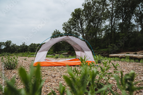 A tent is surrounded by lush green grass in the middle of a wide field, set against a backdrop of tall trees and a sky dotted with fluffy clouds, showcasing the beauty of nature photo