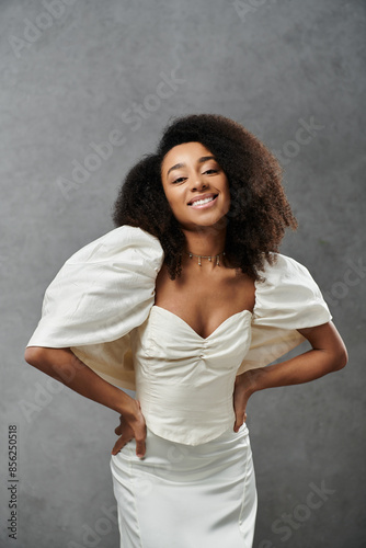 A beautiful African American bride smiles in a white wedding dress, against a gray background.