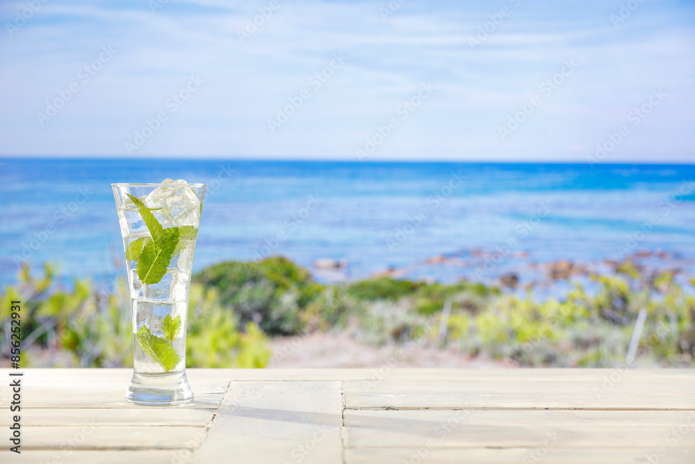 Glass of cold icy mineral water on wooden table top with beautiful landscape of sea and blue sky background. Glass of cold icy mineral water on wooden table top with beautiful landscape of sea and blue sky background.