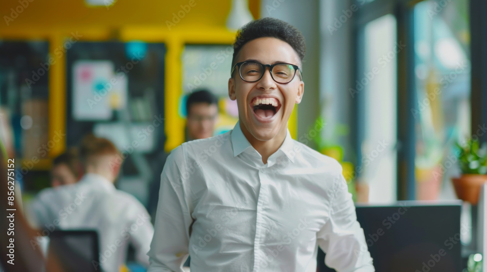 A young man with an exuberant expression, wearing glasses and a white shirt, laughs joyfully in a bright, busy office space. A young man with an exuberant expression, wearing glasses and a white shirt, laughs joyfully in a bright, busy office space.