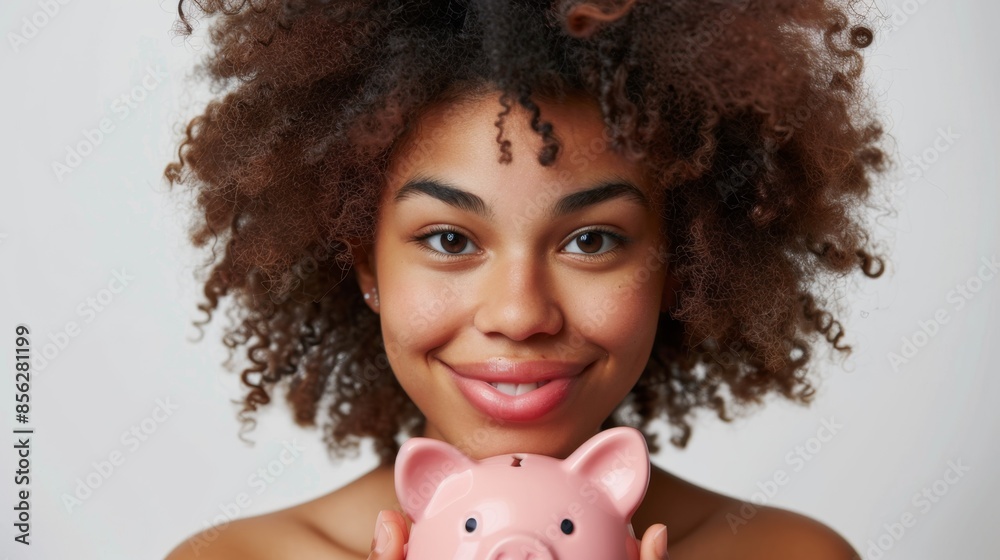 portrait of a beautiful fluffy-haired mulatto young woman holding a pig piggy bank in her hands and looking at the camera with a smile. white studio background. portrait of a beautiful fluffy-haired mulatto young woman holding a pig piggy bank in her hands and looking at the camera with a smile. white studio background.