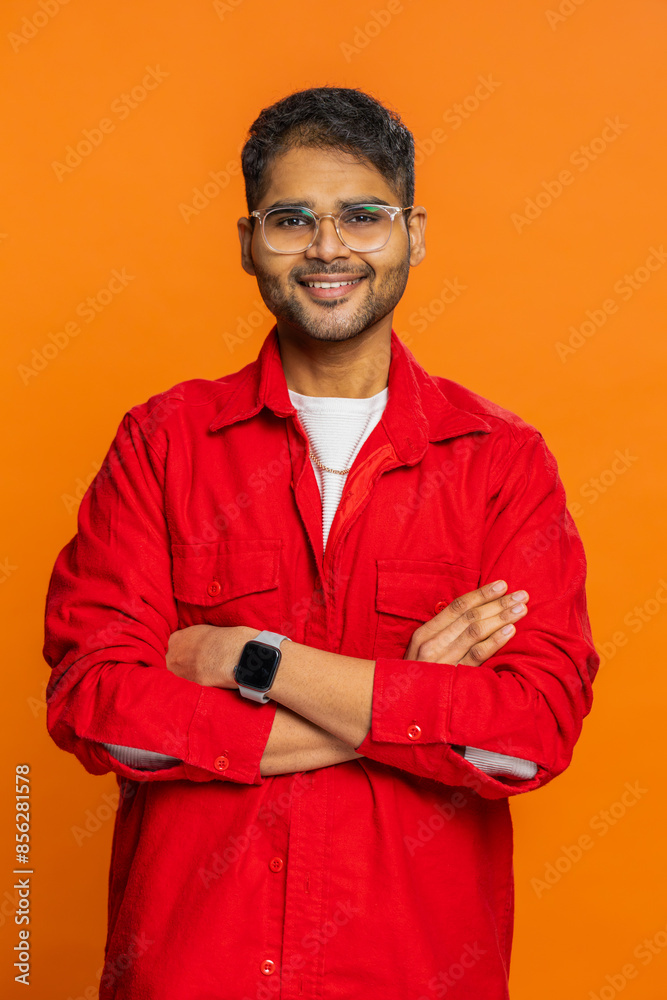 Cheerful happy young Indian man smiling friendly glad expression looking at camera dreaming resting relaxation feel satisfied good news. Arabian guy isolated on orange studio background. Vertical Cheerful happy young Indian man smiling friendly glad expression looking at camera dreaming resting relaxation feel satisfied good news. Arabian guy isolated on orange studio background. Vertical