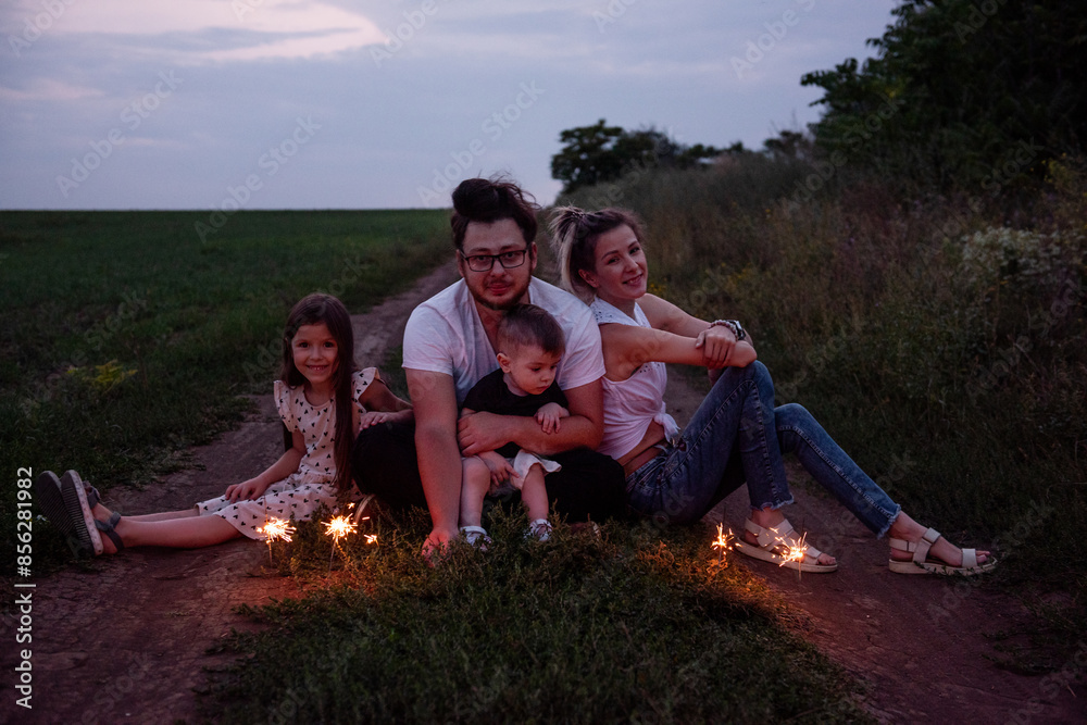 Diversity family of four plays with sparklers on rural path, sharing cozy moment as twilight settles in. Bright celebration in nature Diversity family of four plays with sparklers on rural path, sharing cozy moment as twilight settles in. Bright celebration in nature
