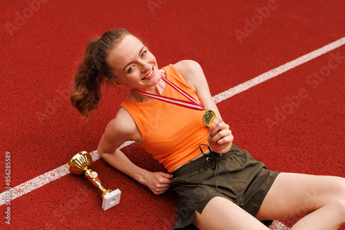 A young female athlete is celebrating her victory with a trophy and medal at the track photo
