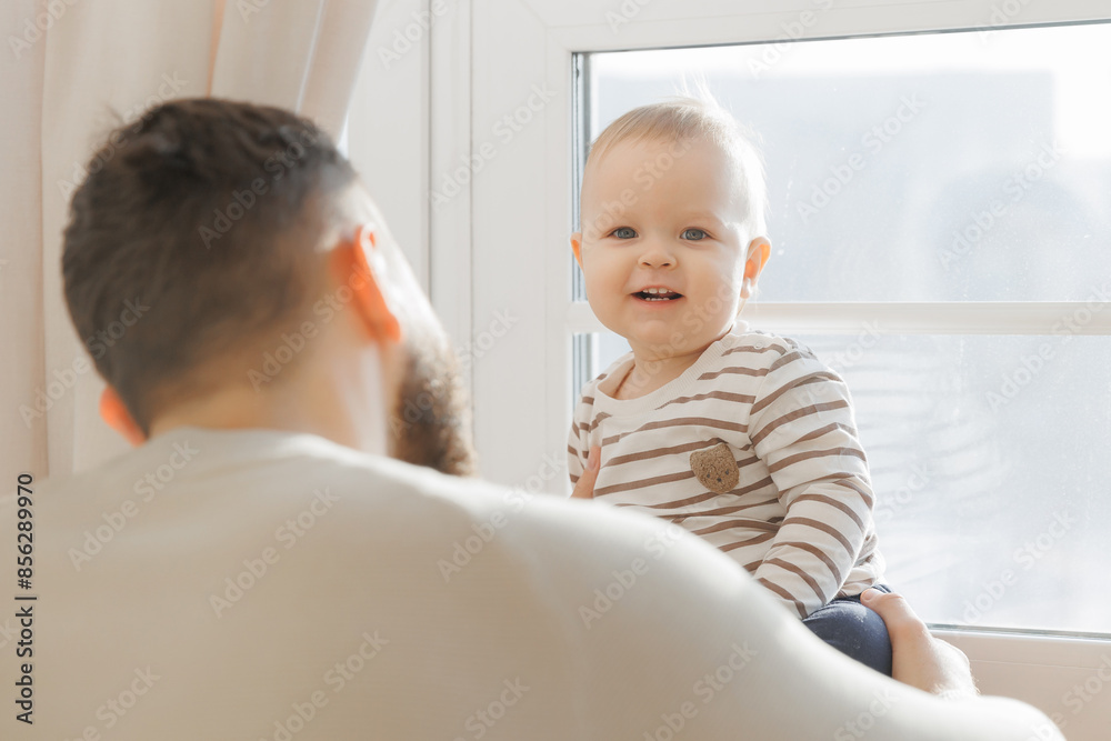 Serene portrait of father baby interaction by window, with dad attentive gaze and little son curious exploration emphasizing familial connection Serene portrait of father baby interaction by window, with dad attentive gaze and little son curious exploration emphasizing familial connection