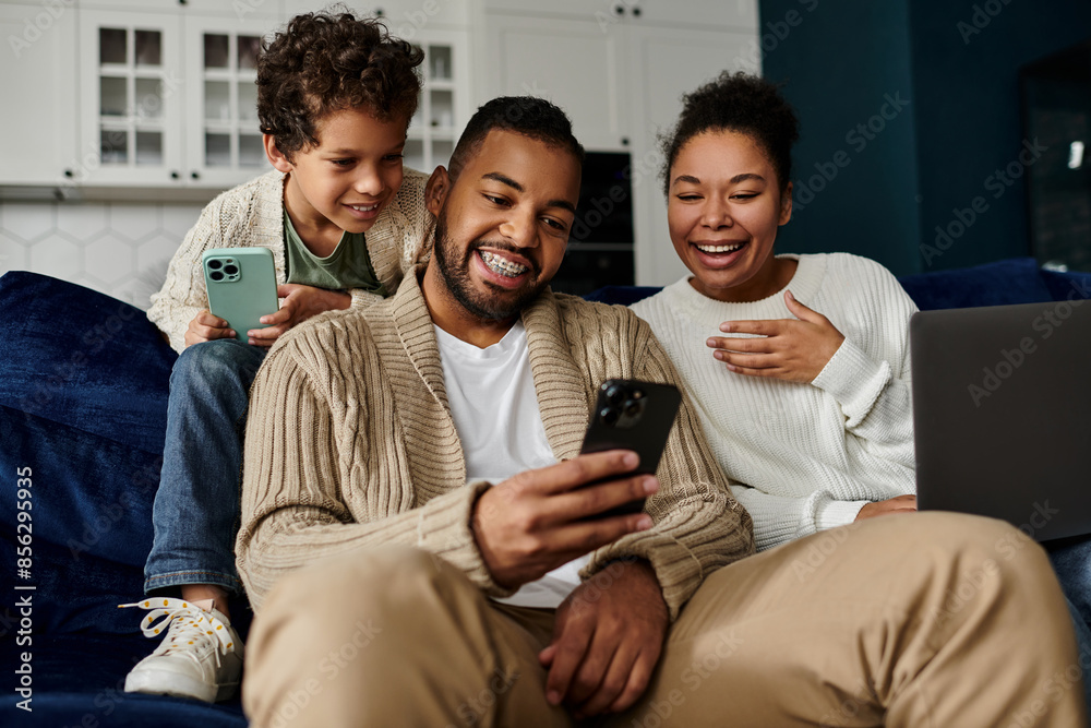 Fototapeta premium African american family engrossed in a cell phone while seated on a couch.