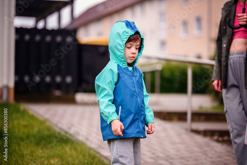 Wallpaper Mural Young child in a teal and blue raincoat, smiling joyfully while standing outdoors on a rainy day. The cheerful expression captures a moment of playful happiness. Torontodigital.ca
