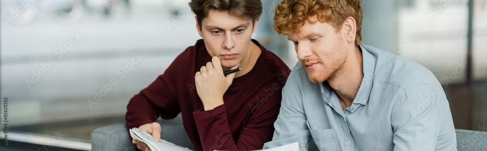 Two male students sit together, reading a paper. Two male students sit together, reading a paper.