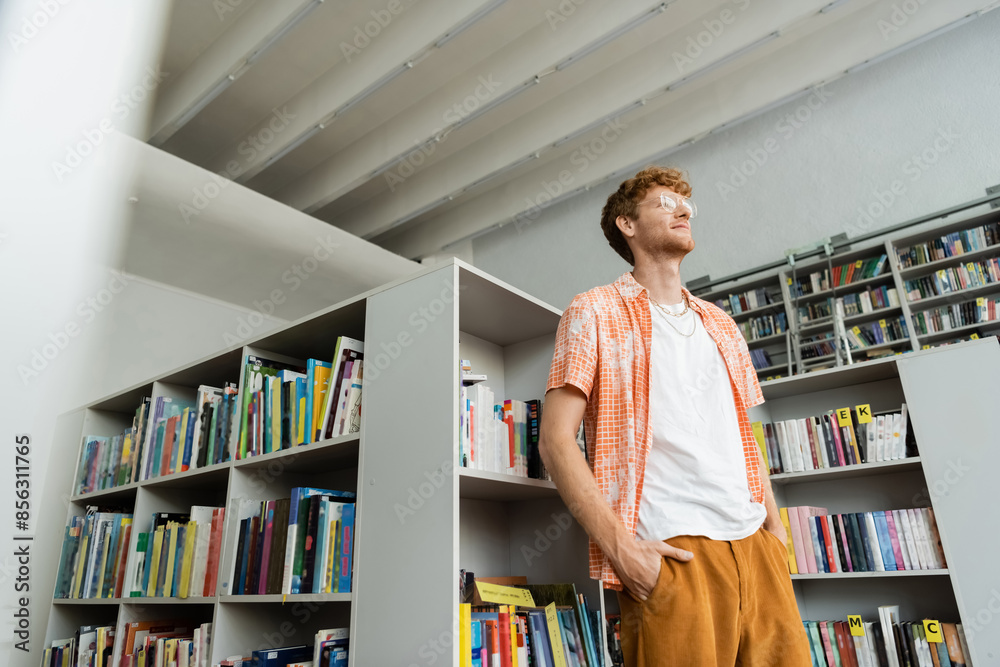 Young man stands before bookshelf full of books in library. Young man stands before bookshelf full of books in library.