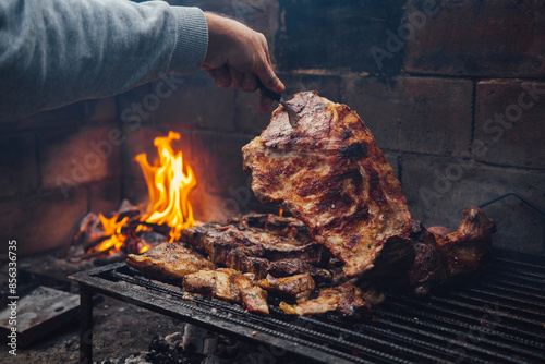 Mature man doing a bbq. He is prodding the meat with a fork. Traditional barbecue called Asado in Argentina.