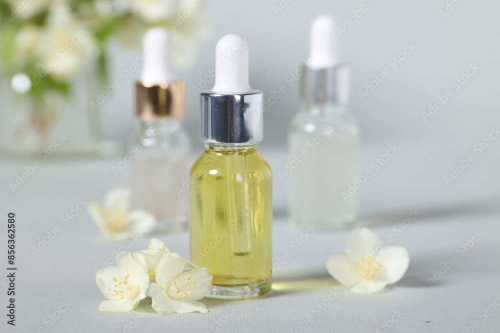 Essential oils in bottles and beautiful jasmine flowers on grey background, closeup Essential oils in bottles and beautiful jasmine flowers on grey background, closeup