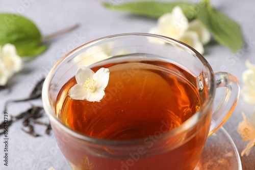 Hot jasmine tea in cup and flowers on light grey table, closeup