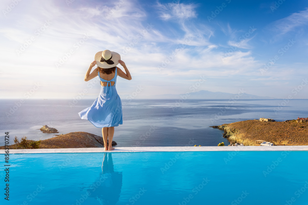 A beautiful summer holiday woman stands by the swimming pool enjoys the sunset over the mediterranean sea, Cyclades, Greece A beautiful summer holiday woman stands by the swimming pool enjoys the sunset over the mediterranean sea, Cyclades, Greece