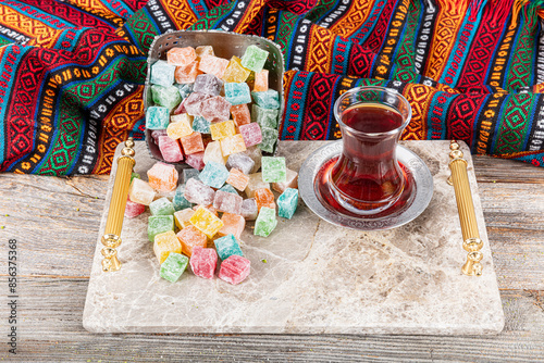 Assorted Turkish delights on a marble tray with a glass of tea. Many colorful sweet Turkish delight in a silver traditional bowl for holiday treats. local name; Meyveli Kus Lokumu. photo