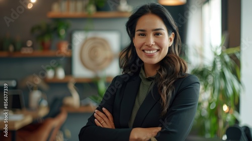 Happy smiling Latin American businesswoman standing in office with arms crossed looking at camera