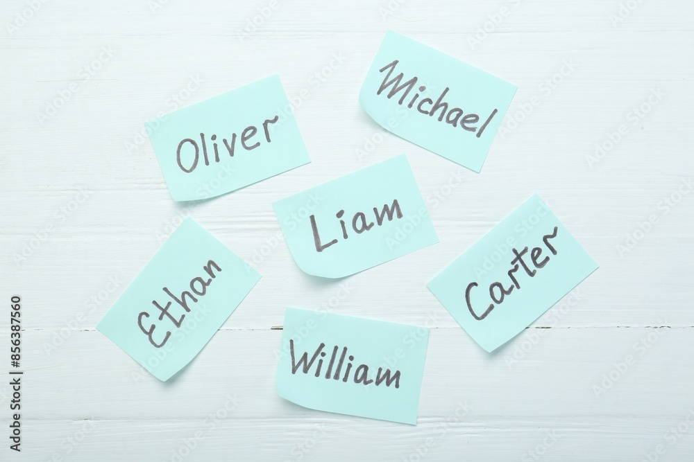 Paper stickers with different names on white wooden background, flat lay. Choosing baby's name Paper stickers with different names on white wooden background, flat lay. Choosing baby's name