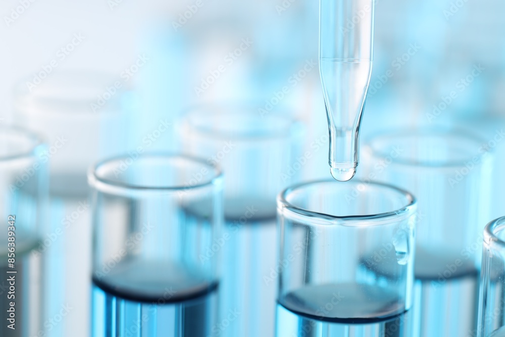 Dripping liquid from pipette into test tube on light background, closeup Dripping liquid from pipette into test tube on light background, closeup