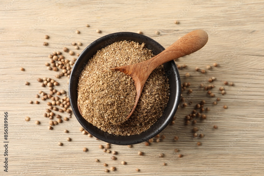 Coriander powder in bowl, spoon and seeds on wooden table, top view
