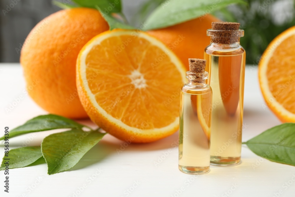 Essential oils in bottles, oranges and green leaves on white table Essential oils in bottles, oranges and green leaves on white table