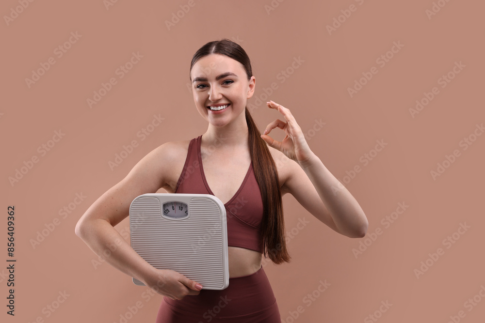 Happy woman with floor scale showing ok gesture on beige background Happy woman with floor scale showing ok gesture on beige background