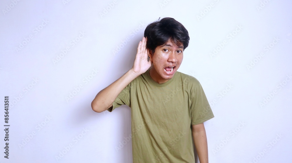 young asian man gestures hand near ear as if listening to something young asian man gestures hand near ear as if listening to something