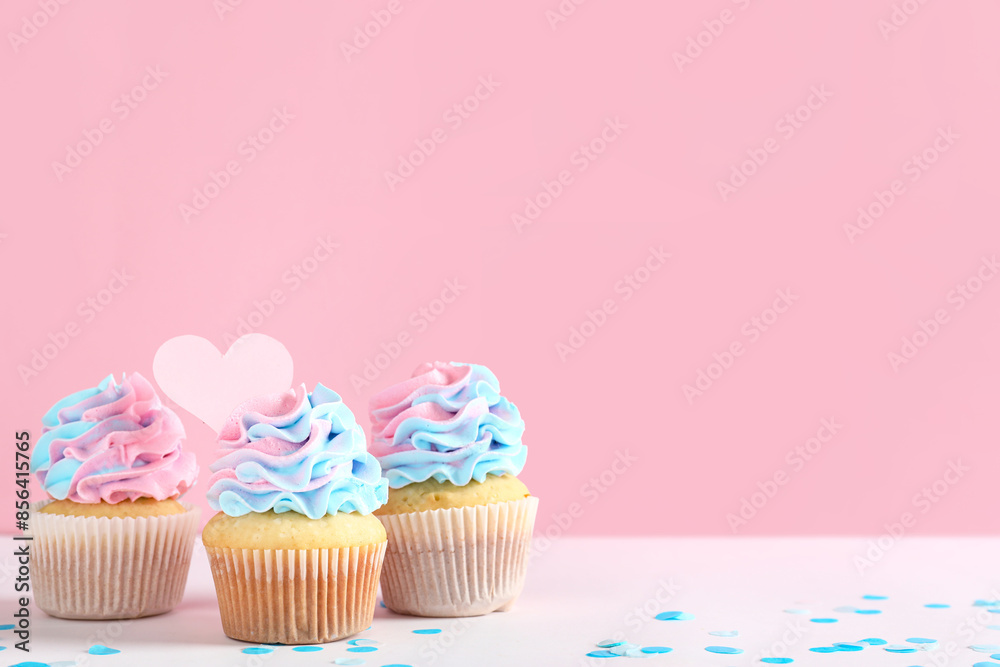 Delicious cupcakes with confetti on table against pink background. Gender reveal party concept Delicious cupcakes with confetti on table against pink background. Gender reveal party concept