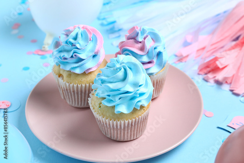 Plate with delicious cupcakes and decorations on blue background. Gender reveal party concept © Pixel-Shot