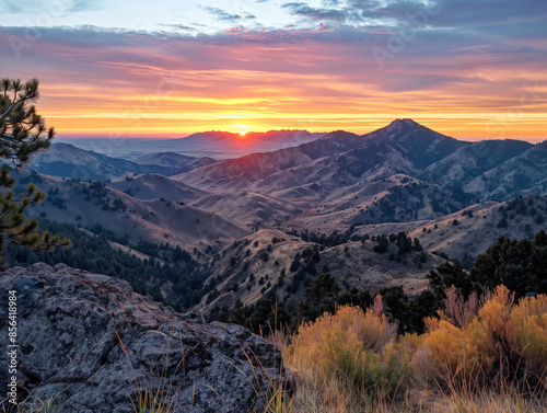 The sun is setting over a mountain range, casting a warm glow over the landscape. The sky is filled with clouds, creating a serene and peaceful atmosphere. The mountains are covered in trees