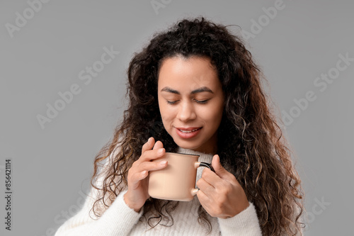 Beautiful young African-American woman with cup of hot mulled wine on grey background