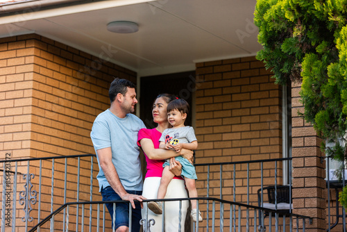 Family of three together on stairs at front of brick home looking at each other