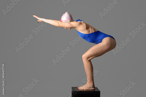 Bilde på lerret Happy young female swimmer on springboard against grey background, side view