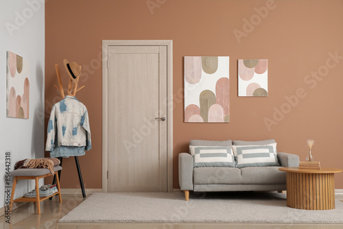 Fototapeta Naklejka Na Ścianę i Meble -  Interior of modern living room with grey sofa, coat rack and stylish pictures hanging on beige wall