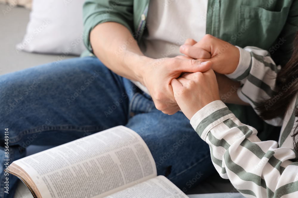 Fototapeta premium Religious couple with Holy Bible praying on sofa at home, closeup