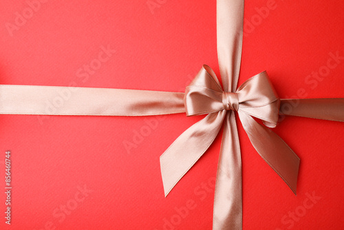 Beige satin ribbon with bow on red background, top view