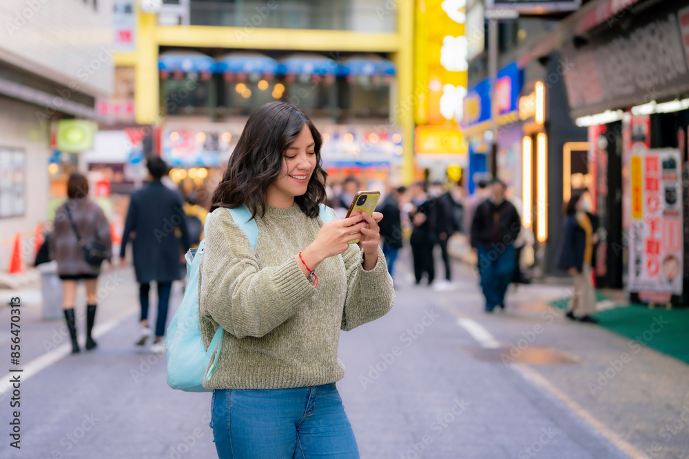A young Latina woman smiles while using her phone on a lively street in Shinjuku, Tokyo, Japan. A young Latina woman smiles while using her phone on a lively street in Shinjuku, Tokyo, Japan.