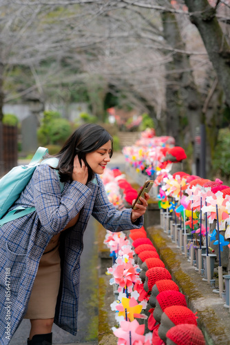 A young Latina woman capturing colorful statues and pinwheels at Zojoji Temple in Tokyo, Japan, using her phone. photo