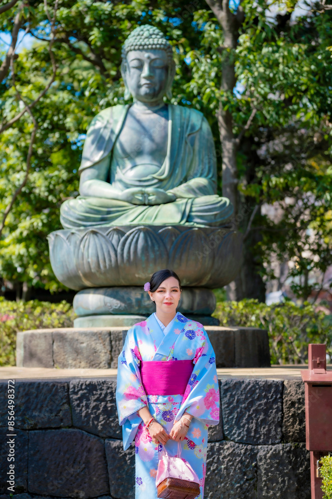 Young Latina woman in a kimono, standing in front of a large Buddha statue in Ueno Park, Tokyo, Japan, enjoying the serene atmosphere. Young Latina woman in a kimono, standing in front of a large Buddha statue in Ueno Park, Tokyo, Japan, enjoying the serene atmosphere.