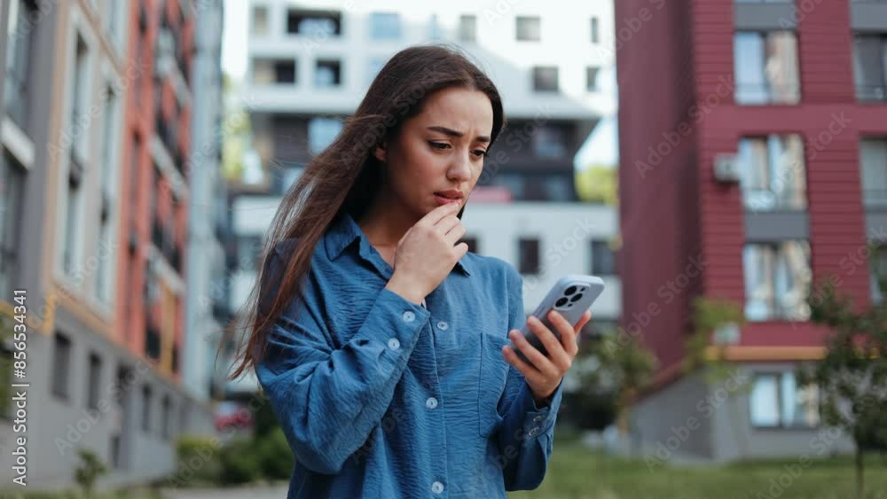 Worried young woman looking stressed while reading a message on her phone.