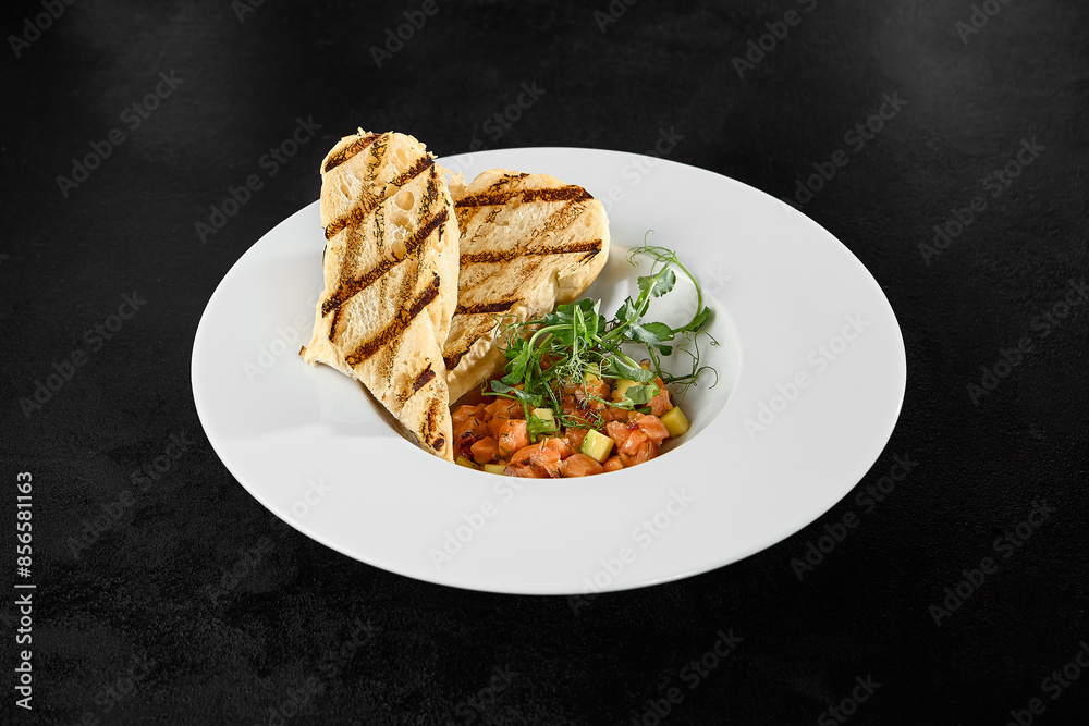 Elegant Salmon Tartar with Avocado, Grilled Ciabatta, and Fresh Greens on Black Background Elegant Salmon Tartar with Avocado, Grilled Ciabatta, and Fresh Greens on Black Background