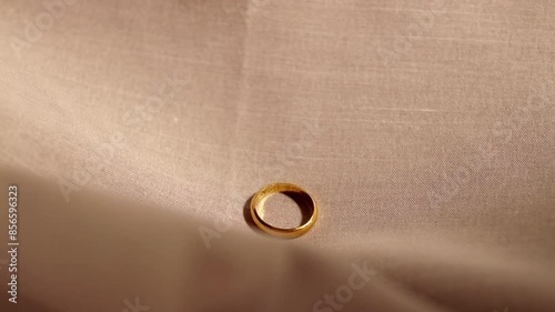 Single gold engagement ring sliding downwards over a tan-colored cotton fabric.