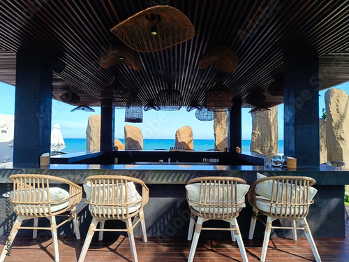 serene and stylish rooftop bar with a stunning ocean view, featuring modern rattan chairs and unique lighting fixtures, perfect for a relaxing getaway