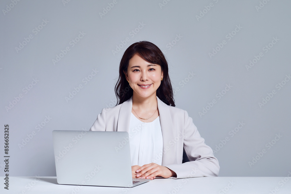カメラ目線のスーツを着た女性とノートパソコン