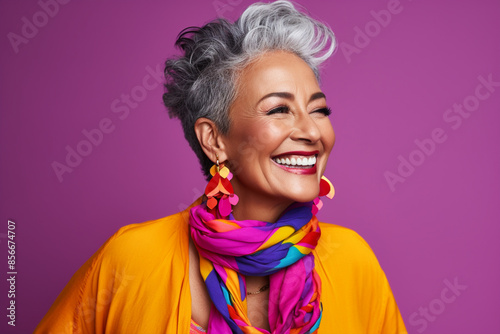Mature middle aged stylish modern woman wearing bright colored neon cloths in purple background, Short hair smiling happy woman wearing fancy jewelries & neck wrapped by a scarf, Granny Model concept