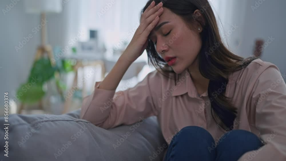 Asian upset depressed woman sitting alone on sofa in living room at home. Asian upset depressed woman sitting alone on sofa in living room at home.