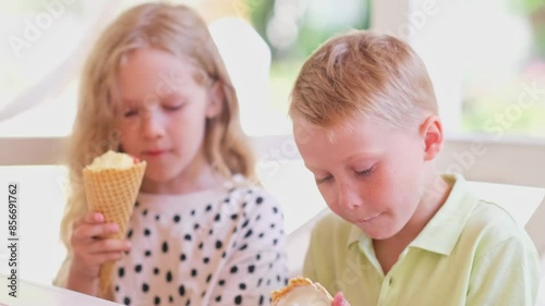 Girl and boy eat and licking ice cream in cone. prescholler friends enthusiastically eating colourful ice cream in cone. The fair-haired brother and sister bought sweet ice cream in cone at a cafe. 4K photo