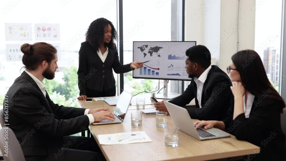 Business meeting with diverse team discussing charts and data analysis. Woman presenting data on screen while colleagues listen and take notes. Professional workspace with city view. Business meeting with diverse team discussing charts and data analysis. Woman presenting data on screen while colleagues listen and take notes. Professional workspace with city view.